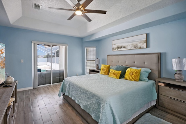 bedroom with ceiling fan, a raised ceiling, hardwood / wood-style flooring, and a textured ceiling