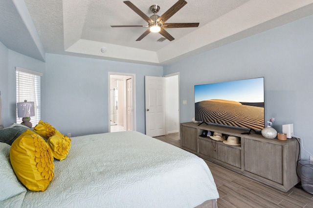 bedroom with ceiling fan, ensuite bath, a textured ceiling, and a tray ceiling