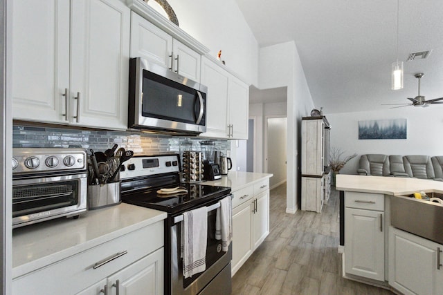 kitchen with white cabinetry, appliances with stainless steel finishes, light hardwood / wood-style floors, tasteful backsplash, and ceiling fan