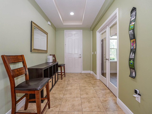 doorway to outside featuring a tray ceiling, french doors, and light tile patterned floors