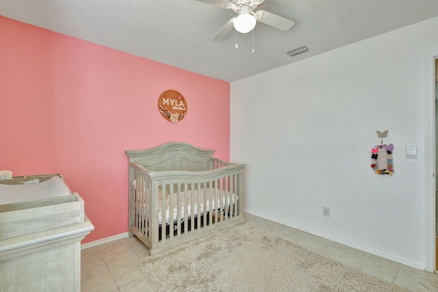 bedroom with a crib, light tile patterned floors, and ceiling fan