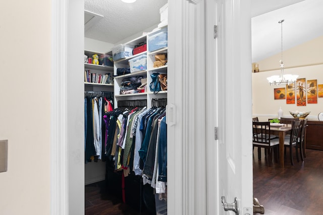 walk in closet with dark wood-type flooring, an inviting chandelier, and vaulted ceiling