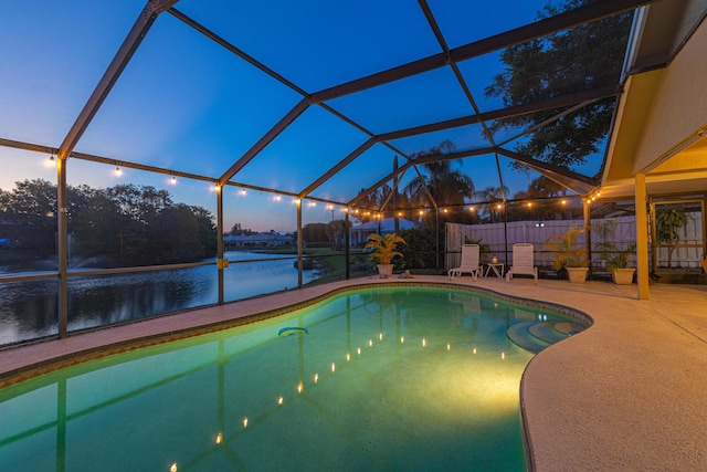 pool at dusk featuring a water view, a patio, and glass enclosure