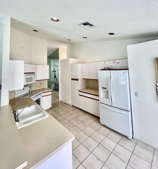 kitchen with a textured ceiling, white appliances, sink, white cabinetry, and light tile patterned flooring