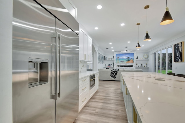 kitchen with white cabinets, appliances with stainless steel finishes, light stone counters, light hardwood / wood-style floors, and decorative light fixtures