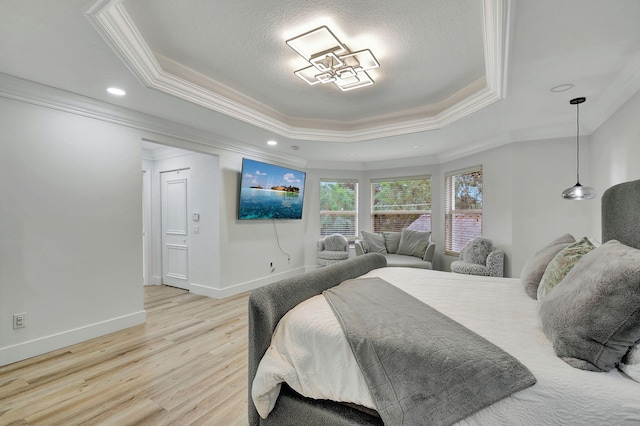 bedroom featuring light wood-type flooring, ornamental molding, a textured ceiling, and a tray ceiling