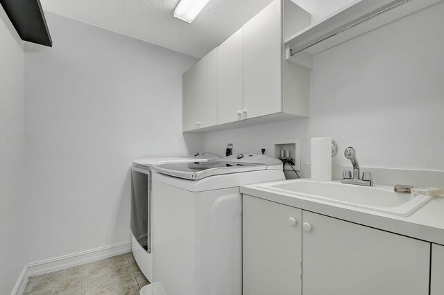 clothes washing area with separate washer and dryer, sink, light tile patterned flooring, and cabinets