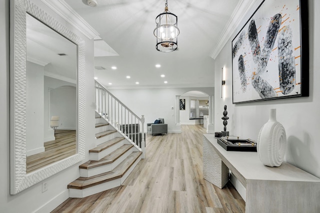 entryway with a notable chandelier, ornamental molding, and light wood-type flooring