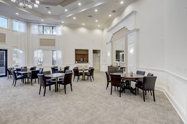 carpeted dining room with a towering ceiling, crown molding, and a chandelier