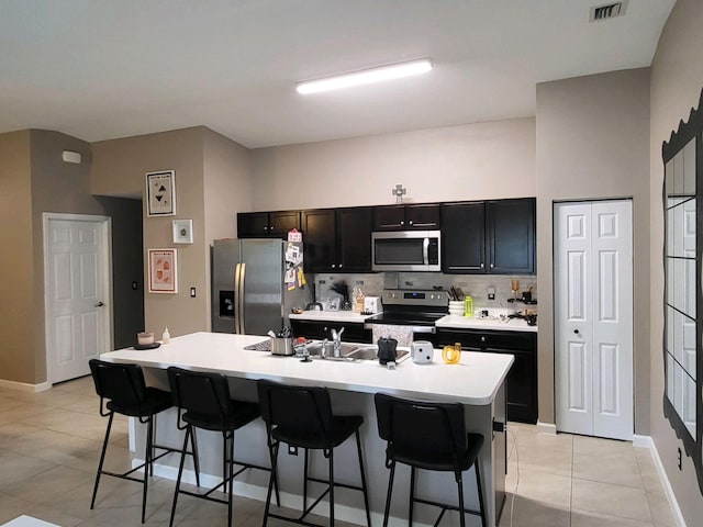 kitchen with tasteful backsplash, an island with sink, light tile patterned flooring, a breakfast bar, and appliances with stainless steel finishes