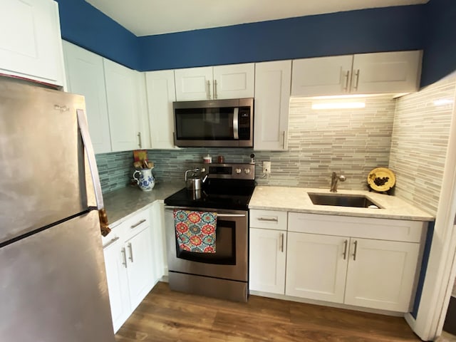 kitchen with white cabinetry, a sink, stainless steel appliances, decorative backsplash, and dark wood-style floors