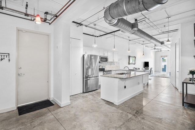 kitchen with white cabinets, appliances with stainless steel finishes, an island with sink, and a towering ceiling