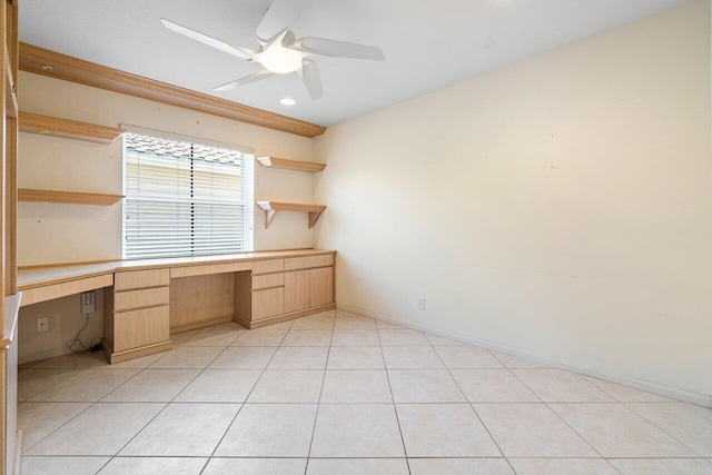 unfurnished office with ceiling fan, light tile patterned flooring, and built in desk