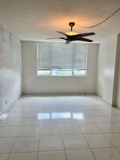 empty room featuring a textured ceiling, light tile patterned flooring, and ceiling fan