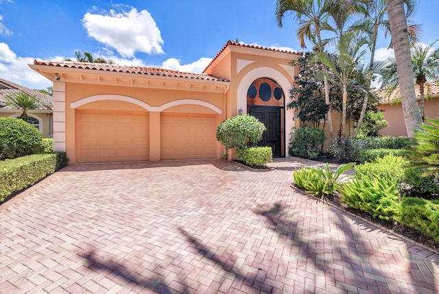 mediterranean / spanish-style home featuring a garage, decorative driveway, and stucco siding