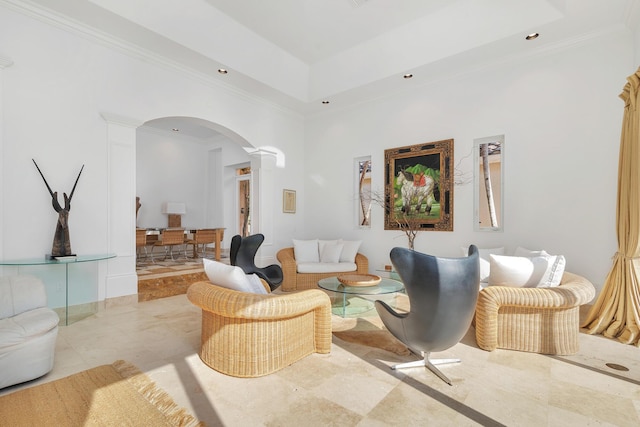 living area featuring arched walkways, ornamental molding, a tray ceiling, ornate columns, and recessed lighting