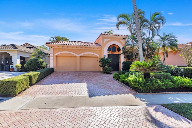 mediterranean / spanish-style home featuring an attached garage, a tiled roof, decorative driveway, and stucco siding