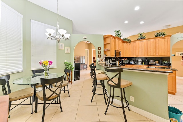 kitchen with kitchen peninsula, light tile patterned floors, backsplash, hanging light fixtures, and a notable chandelier