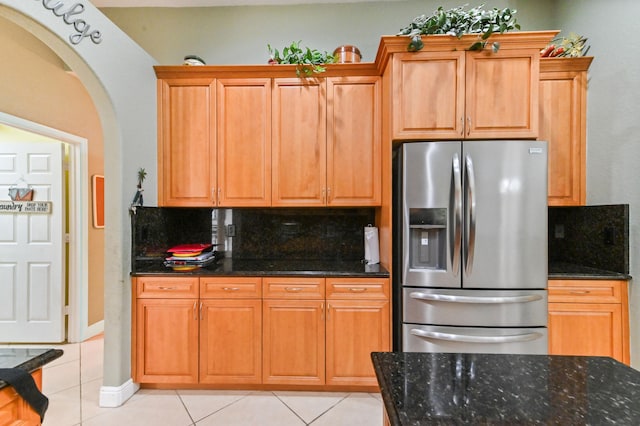 kitchen with dark stone counters, tasteful backsplash, light tile patterned floors, and stainless steel fridge