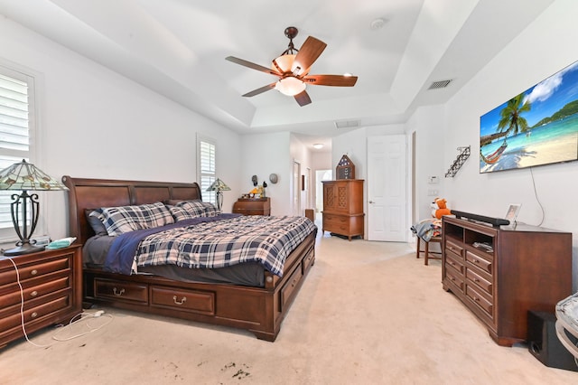 bedroom featuring a tray ceiling, light colored carpet, and ceiling fan