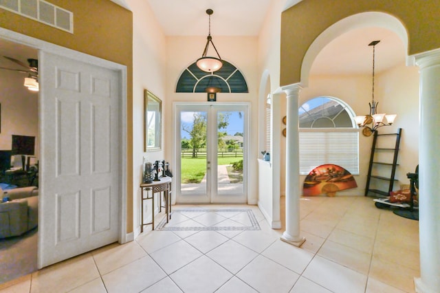 entryway featuring ornate columns, ceiling fan with notable chandelier, light tile patterned floors, and a high ceiling