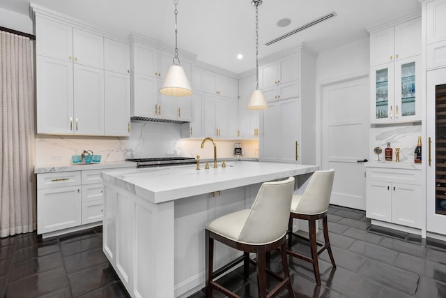 kitchen with white cabinets, decorative backsplash, and a center island with sink