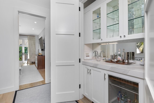 bar featuring white cabinets, sink, wine cooler, light stone countertops, and light hardwood / wood-style floors