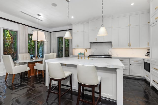 kitchen with decorative backsplash, a kitchen island with sink, white cabinetry, hanging light fixtures, and a breakfast bar area