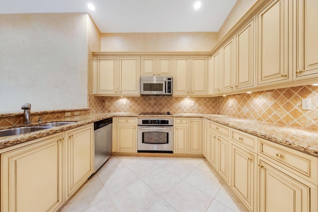 kitchen featuring light stone countertops, sink, backsplash, cream cabinets, and appliances with stainless steel finishes