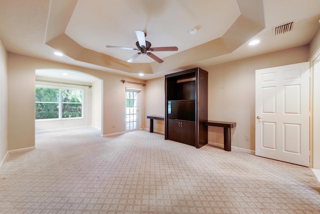 unfurnished living room featuring a raised ceiling, light carpet, and ceiling fan