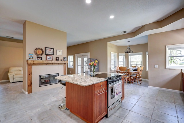 kitchen featuring stainless steel electric stove, light tile patterned floors, a fireplace, a breakfast bar area, and decorative light fixtures