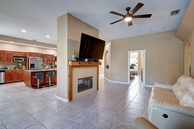 living room featuring ceiling fan, a fireplace, and light tile patterned flooring