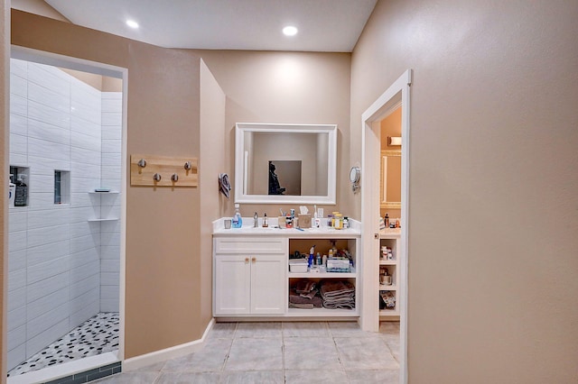 bathroom featuring tile patterned flooring, a tile shower, and vanity