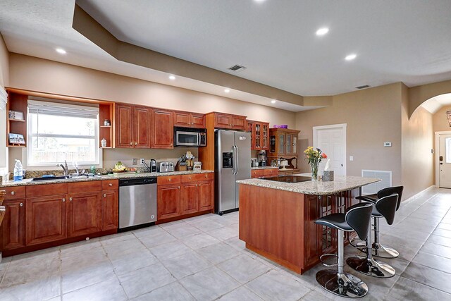 kitchen featuring a center island, sink, appliances with stainless steel finishes, light stone counters, and light tile patterned floors