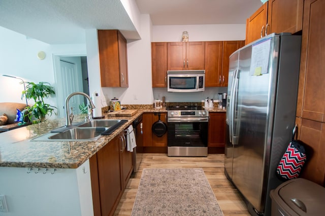 kitchen with light hardwood / wood-style floors, light stone counters, sink, and appliances with stainless steel finishes