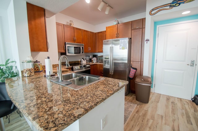 kitchen featuring stone counters, sink, light hardwood / wood-style flooring, appliances with stainless steel finishes, and kitchen peninsula