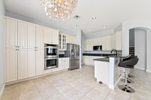 kitchen featuring a kitchen bar, stainless steel appliances, light tile patterned floors, and a chandelier