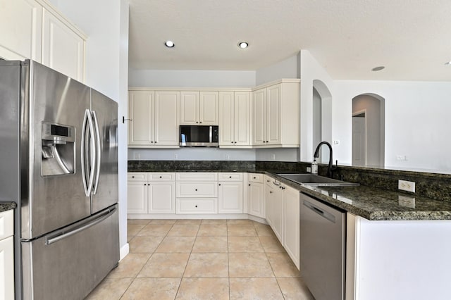 kitchen with stainless steel appliances, light tile patterned flooring, sink, dark stone countertops, and a textured ceiling