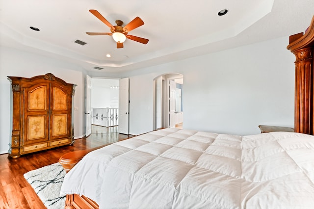 bedroom with wood-type flooring, ceiling fan, and a raised ceiling