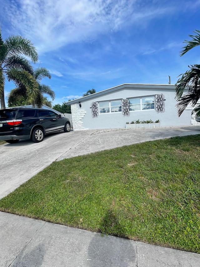 view of side of home featuring stucco siding, a lawn, and concrete driveway