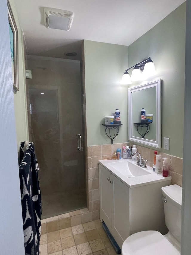 bathroom with tiled shower, toilet, vanity, and tile walls