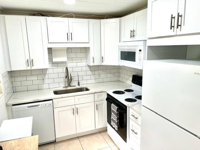 kitchen with white cabinetry, sink, light tile patterned floors, and white appliances