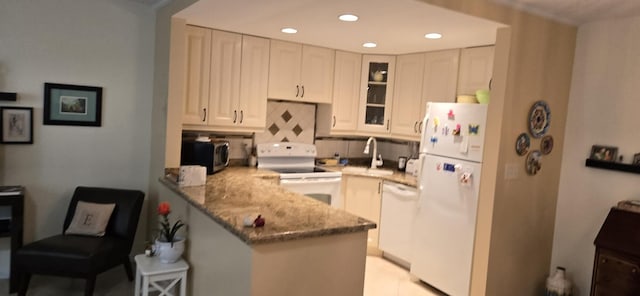 kitchen with backsplash, light stone counters, a kitchen breakfast bar, kitchen peninsula, and white appliances