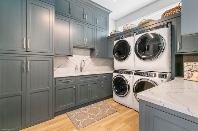 laundry room featuring light wood-type flooring, sink, stacked washer and dryer, cabinets, and washer and clothes dryer