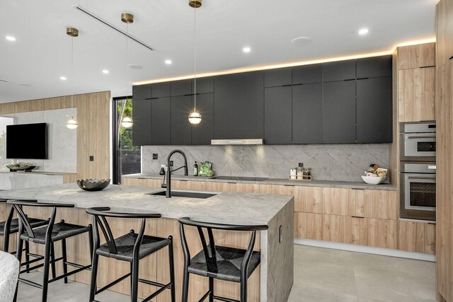 kitchen with stainless steel double oven, a kitchen island with sink, pendant lighting, tasteful backsplash, and a breakfast bar