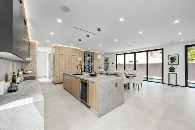 kitchen with hanging light fixtures, light tile patterned floors, sink, beverage cooler, and a center island with sink