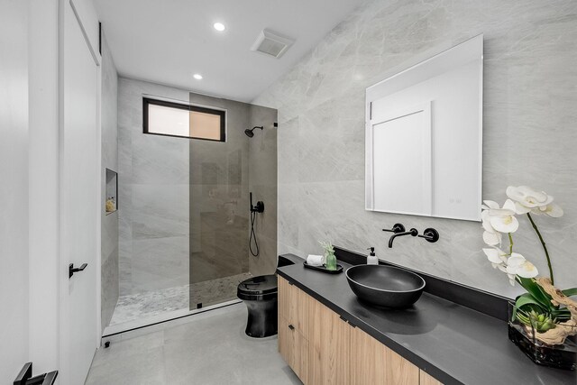 bathroom featuring toilet, tile patterned flooring, vanity, a tile shower, and tile walls