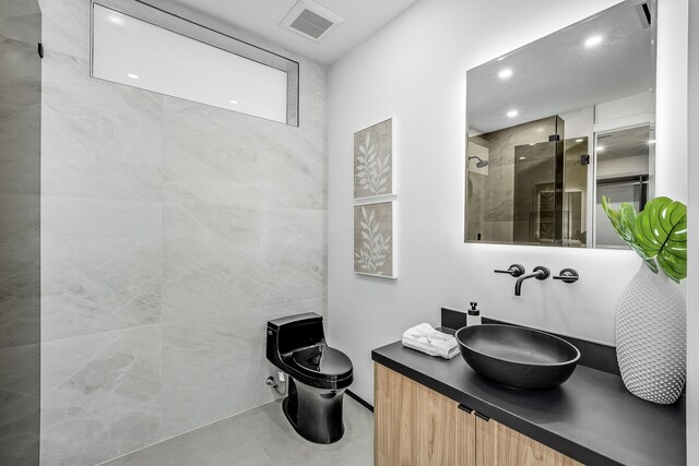 bathroom featuring toilet, tile patterned flooring, vanity, a tile shower, and tile walls