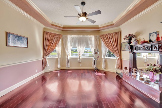 interior space with ceiling fan, a raised ceiling, ornamental molding, and dark hardwood / wood-style flooring