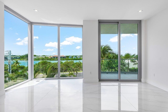 empty room featuring a water view, light tile patterned floors, and a wall of windows